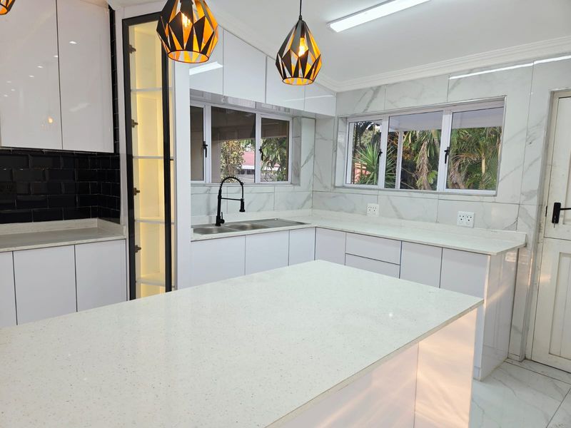 Modern, renovated kitchen featuring white glossy cabinetry, quartz countertops, a central island, and elegant marble-look wall tiling with a contrasting black backsplash.