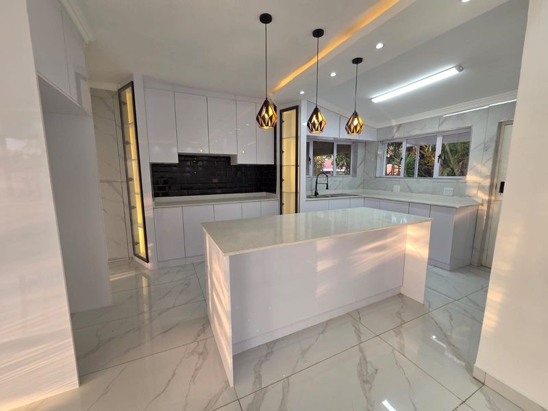 Modern, renovated kitchen featuring a central island, white cabinetry, quartz countertops, marble-look floor tiles, and stylish pendant lighting.