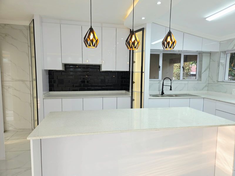 Modern, high-end kitchen featuring sleek white cabinetry, contrasting black subway tile backsplash, quartz countertops, and contemporary pendant lighting.