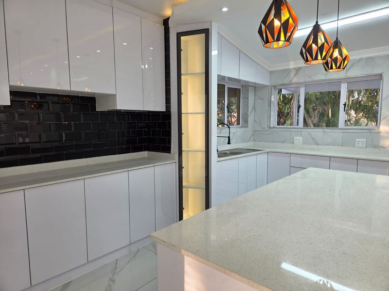 Modern kitchen featuring high-gloss white cabinetry, quartz countertops, a striking black subway tile backsplash, and integrated display shelving with marble-look flooring.