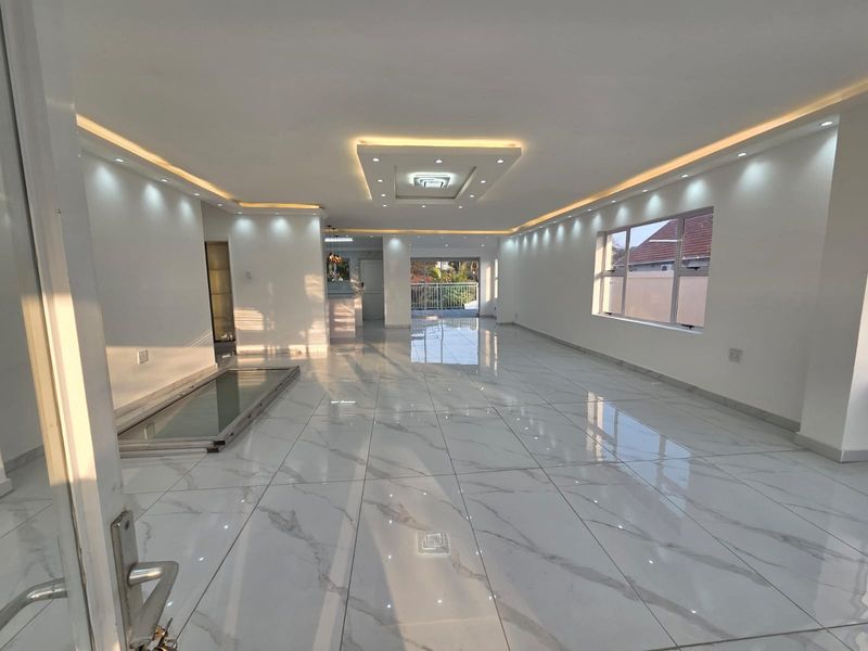 Spacious open-plan living area featuring modern recessed ceiling lighting, cove lighting, and polished marble-look porcelain floor tiles throughout.