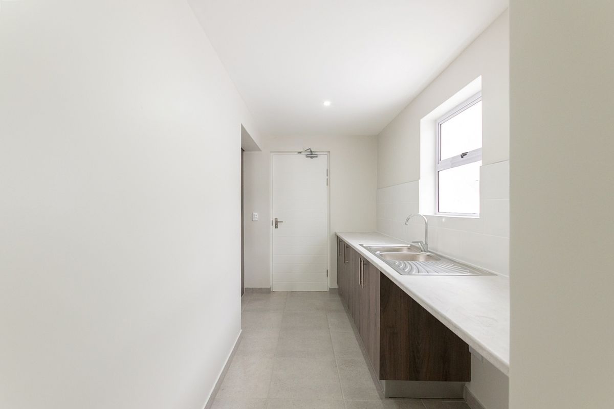 A clean and functional scullery featuring modern cabinetry, a stainless steel sink, and tiled flooring, providing a practical secondary workspace.