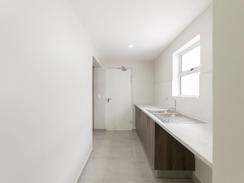 A clean and functional scullery featuring modern cabinetry, a stainless steel sink, and tiled flooring, providing a practical secondary workspace.