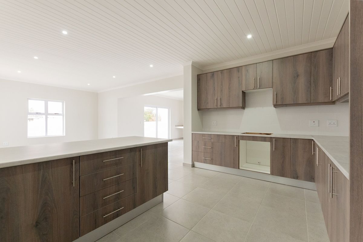 Modern open-plan kitchen featuring wood-look cabinetry, a central island, and tiled flooring, seamlessly flowing into the adjacent living area.