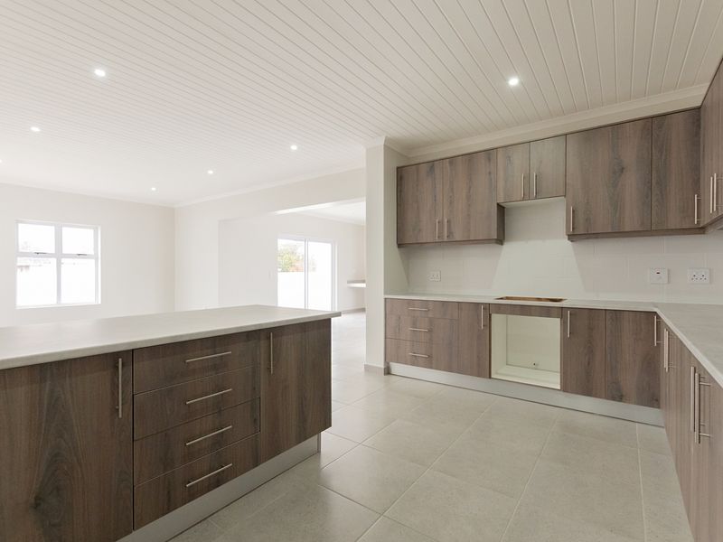 Modern open-plan kitchen featuring wood-look cabinetry, a central island, and tiled flooring, seamlessly flowing into the adjacent living area.