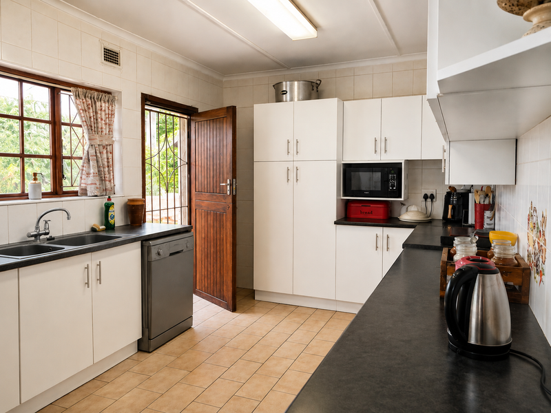 A functional kitchen featuring white cabinetry, dark countertops, tiled splashbacks, and direct access to the exterior through a wooden door.