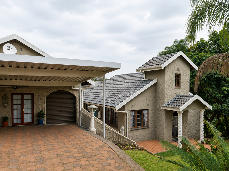 Front elevation of a house featuring a paved driveway, attached carport, garage, and textured facade with classic architectural details.