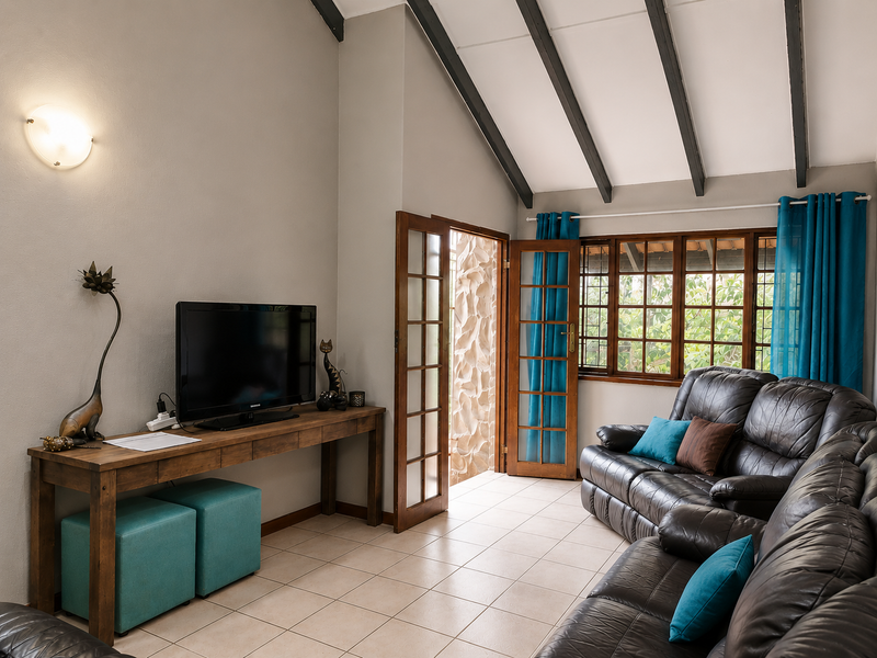 A cozy living room featuring exposed timber ceiling beams, tiled flooring, and direct access to an outdoor area through timber-framed glass doors.