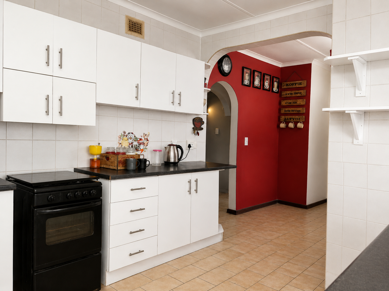 A functional kitchen featuring white cabinetry, black countertops, a freestanding oven, and ceramic tiling, leading into an arched transition area with a red accent wall.