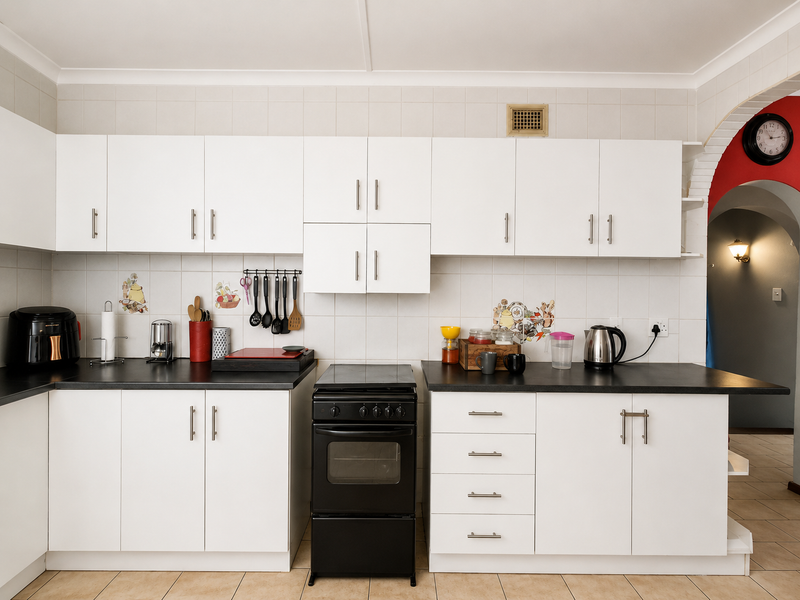 A clean, functional kitchen featuring white cabinetry, black countertops, a freestanding stove, and a tiled backsplash, leading into an arched entryway.