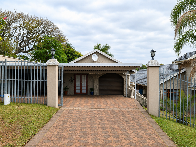 Front view of the property featuring a paved driveway, covered carport, secure metal gate, and garage access.