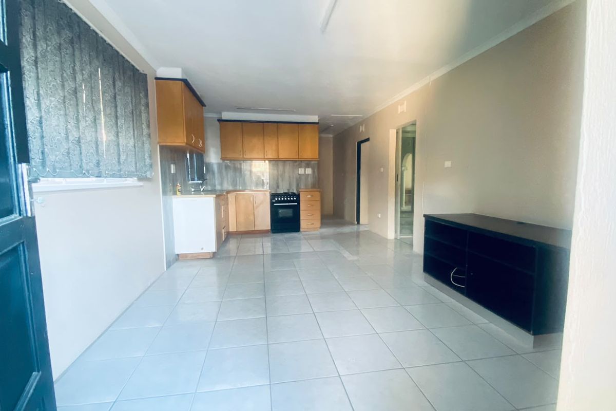 Open-plan living and kitchen area featuring tiled flooring, wooden cabinetry, and a freestanding stove, offering a functional and versatile layout.