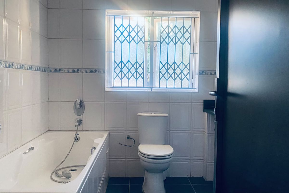 A functional bathroom featuring a built-in bathtub, toilet, and tiled finishes, complete with a security gate on the window.