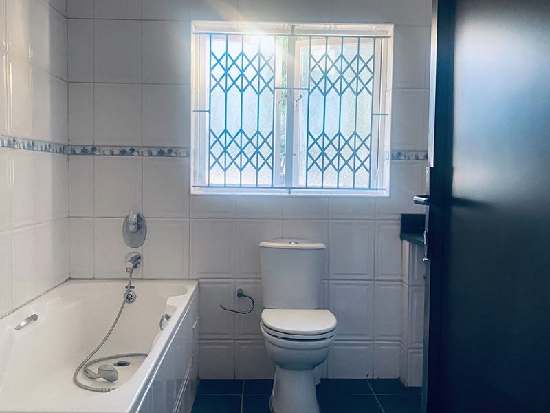 A functional bathroom featuring a built-in bathtub, toilet, and tiled finishes, complete with a security gate on the window.