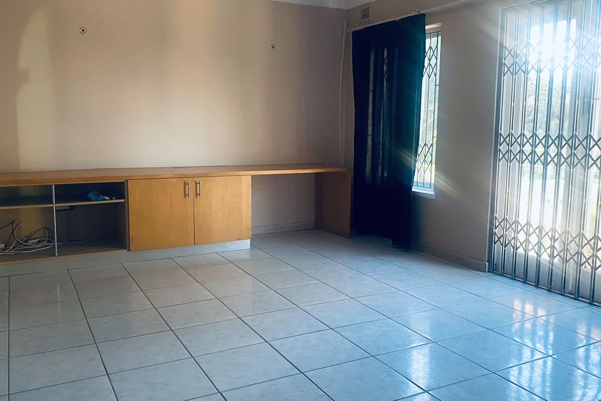 An empty living room featuring tiled flooring, built-in cabinetry, and a security gate leading to an outdoor area.