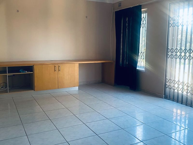 An empty living room featuring tiled flooring, built-in cabinetry, and a security gate leading to an outdoor area.