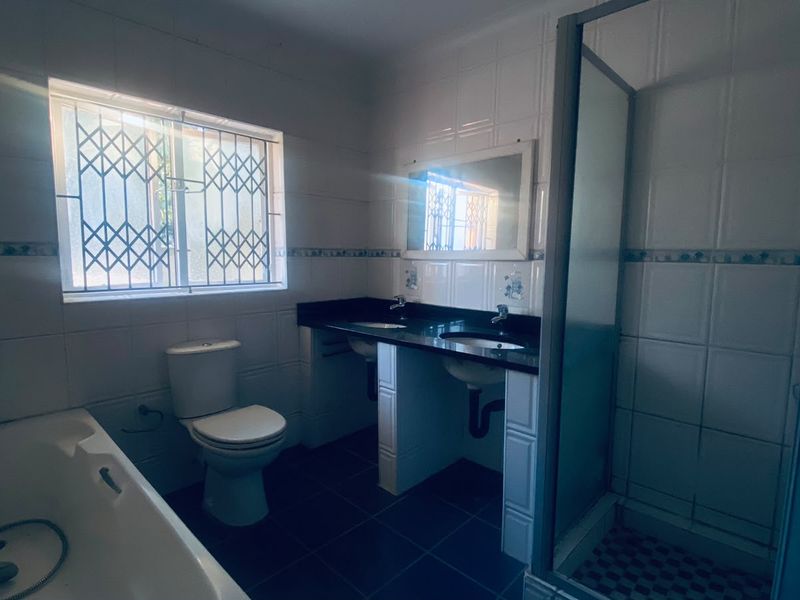 A functional bathroom featuring a built-in bathtub, separate shower enclosure, and a double vanity with dark countertops and tiled finishes.