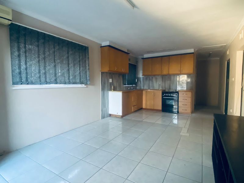 Open-plan living and kitchen area featuring tiled flooring, built-in cabinetry, and a wall-mounted air conditioning unit in a neutral, functional space.