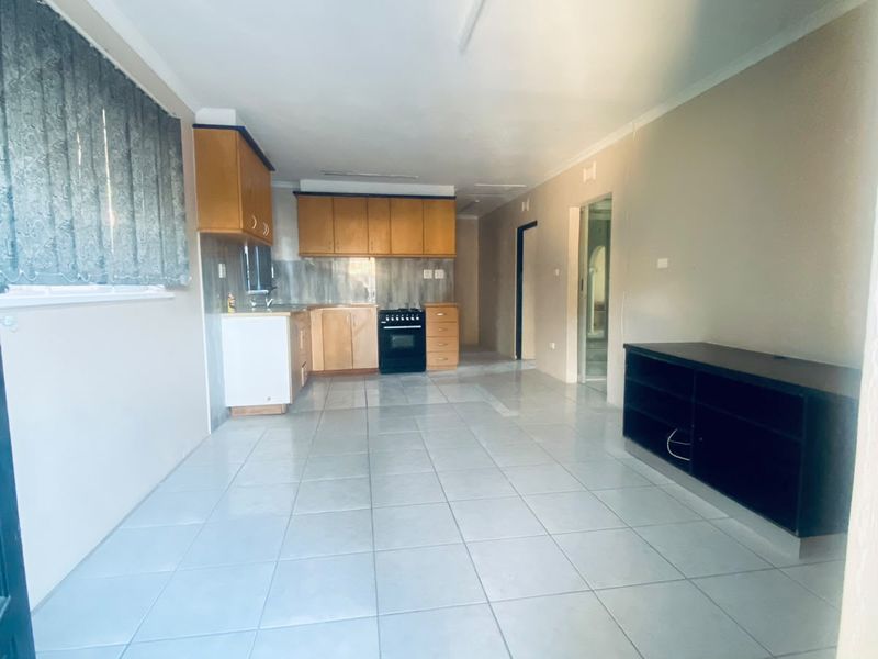 Open-plan living and kitchen area featuring tiled flooring, wooden cabinetry, and a freestanding stove, offering a functional and versatile layout.
