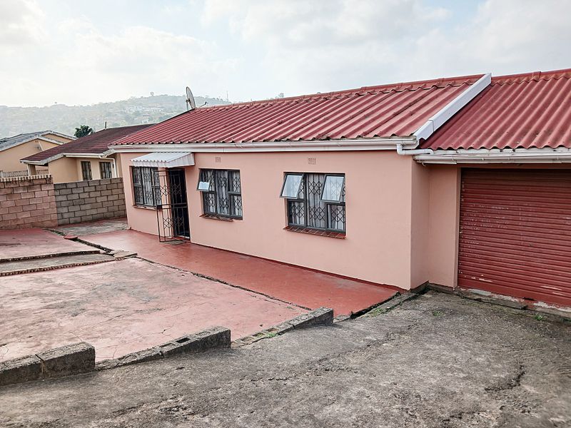 Front elevation of a single-story house featuring a corrugated metal roof, security-fitted windows, a roller garage door, and a paved driveway area.