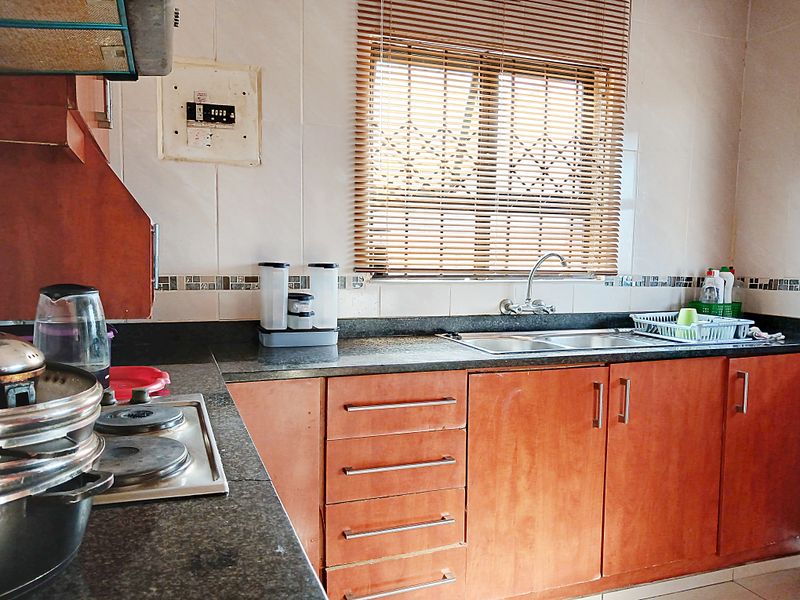 A functional kitchen featuring wooden cabinetry, granite countertops, a stainless steel sink, and an integrated electric hob with an extractor fan.