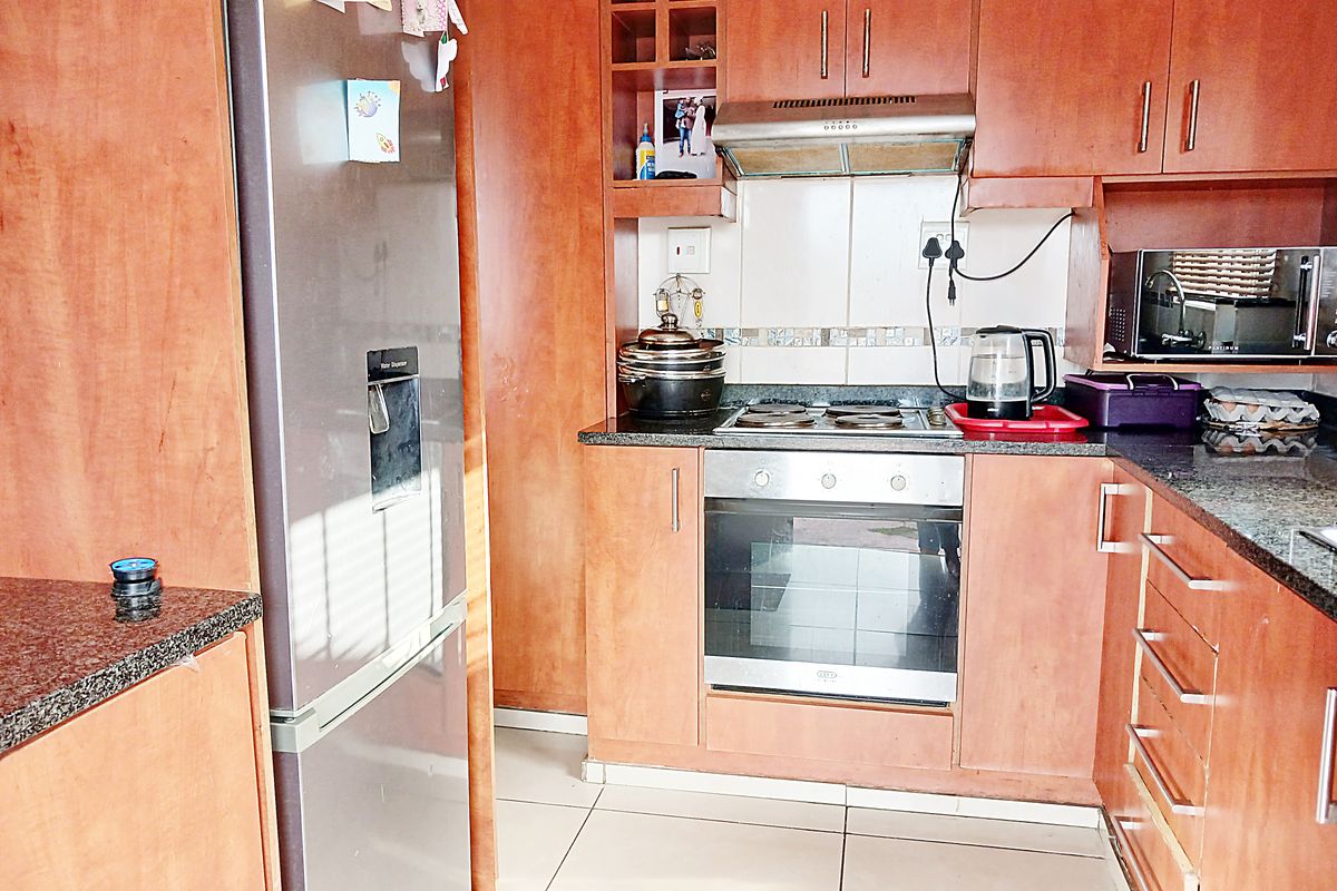 A functional kitchen featuring wood-finish cabinetry, granite countertops, a built-in oven, electric hob, and an extractor fan with tiled flooring.