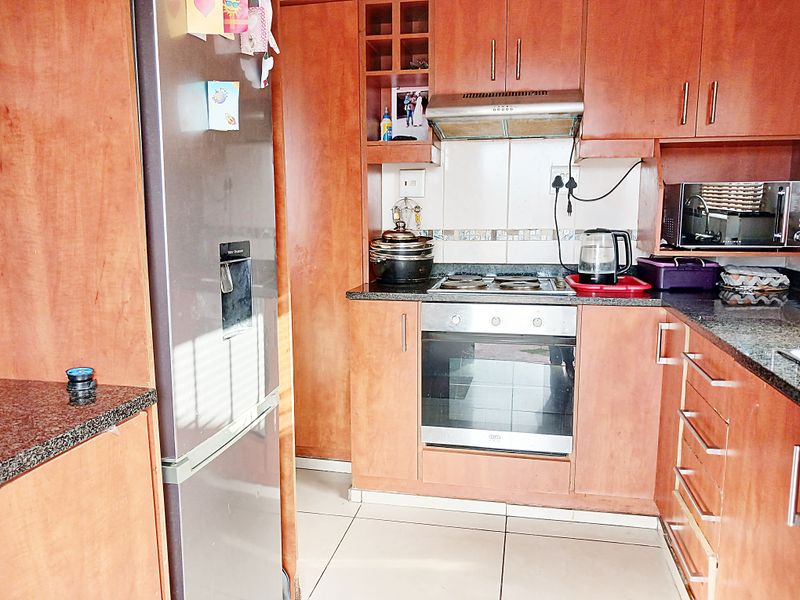 A functional kitchen featuring wood-finish cabinetry, granite countertops, a built-in oven, electric hob, and an extractor fan with tiled flooring.