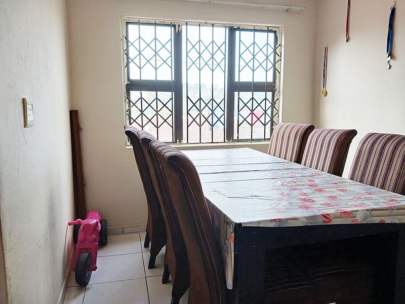 A dining room featuring tiled flooring and a window with a fitted security gate, showing signs of wear on the walls.