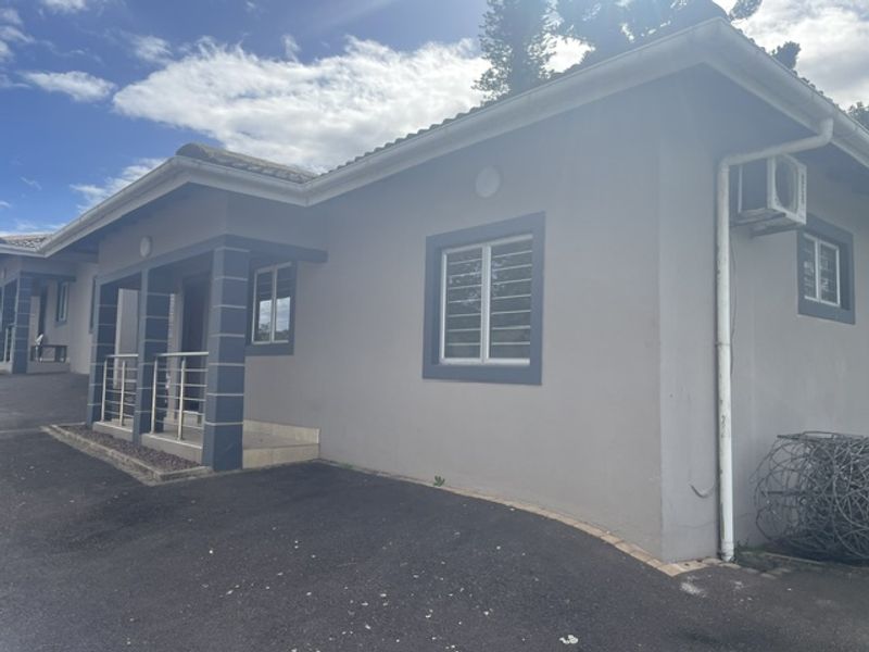 Front exterior view of the townhouse featuring a paved driveway, covered entrance porch with stainless steel balustrade, and security bars on windows.
