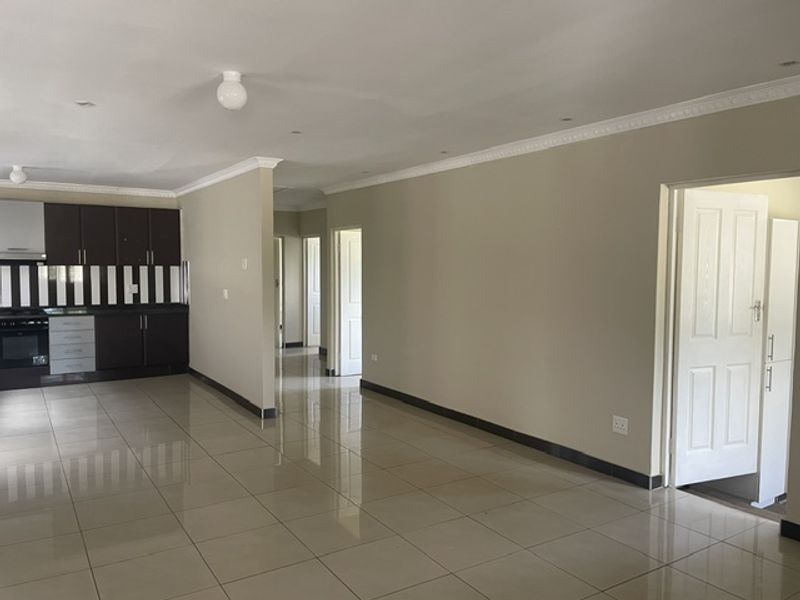 Spacious open-plan living area featuring large format floor tiles, recessed lighting, and a modern kitchen with built-in cabinetry and appliances.