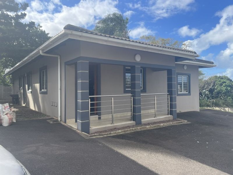 Front elevation of a townhouse featuring a covered patio with stainless steel balustrades, paved driveway, and secure window bars.
