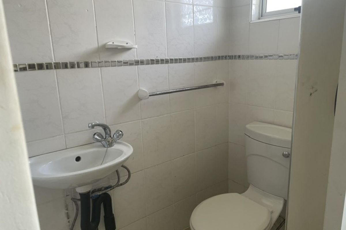 A compact bathroom featuring a wall-mounted basin, chrome mixer tap, and standard toilet with white ceramic wall tiling.