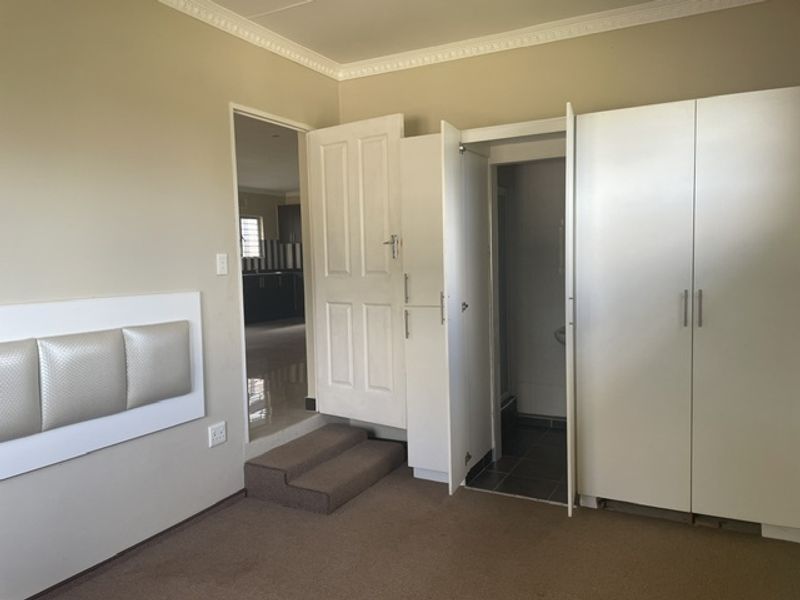 A spacious bedroom featuring built-in cupboards, crown molding, and direct access to an en-suite bathroom.