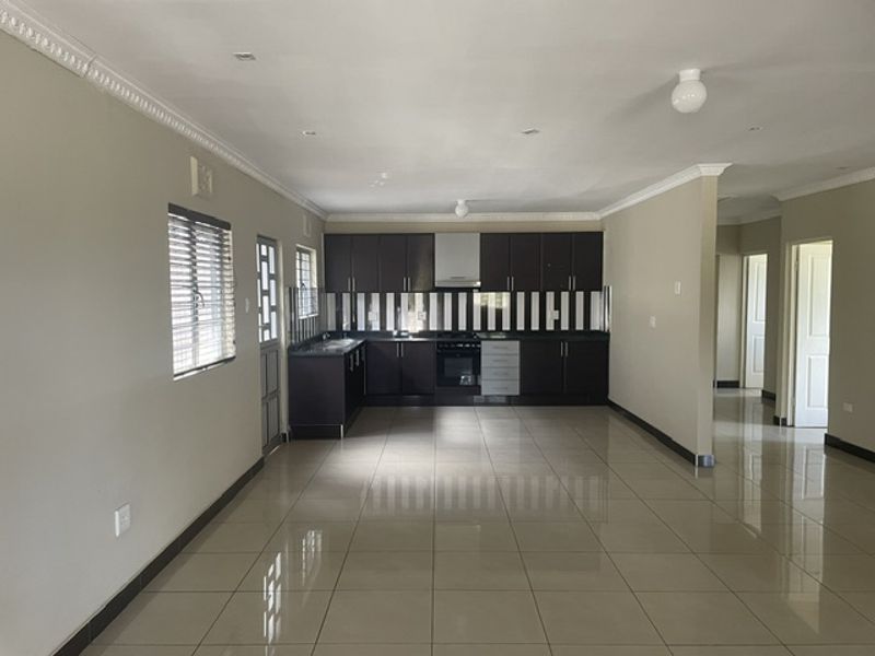 Spacious open-plan kitchen and living area featuring dark cabinetry, built-in appliances, and neutral ceramic tile flooring throughout.