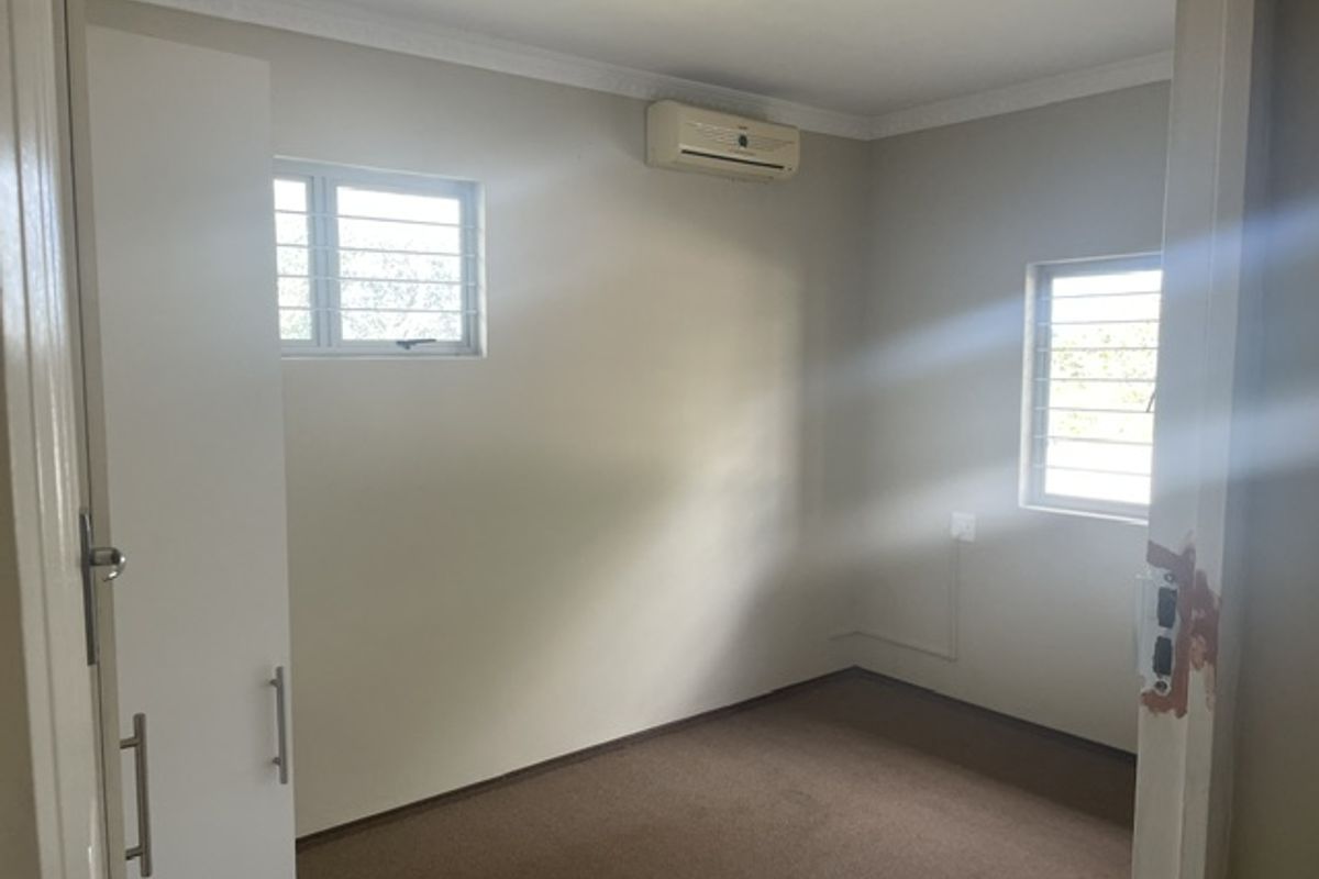 A clean, empty bedroom featuring built-in cupboards, an air conditioning unit, and security bars on the windows.
