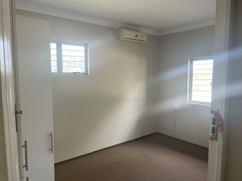 A clean, empty bedroom featuring built-in cupboards, an air conditioning unit, and security bars on the windows.