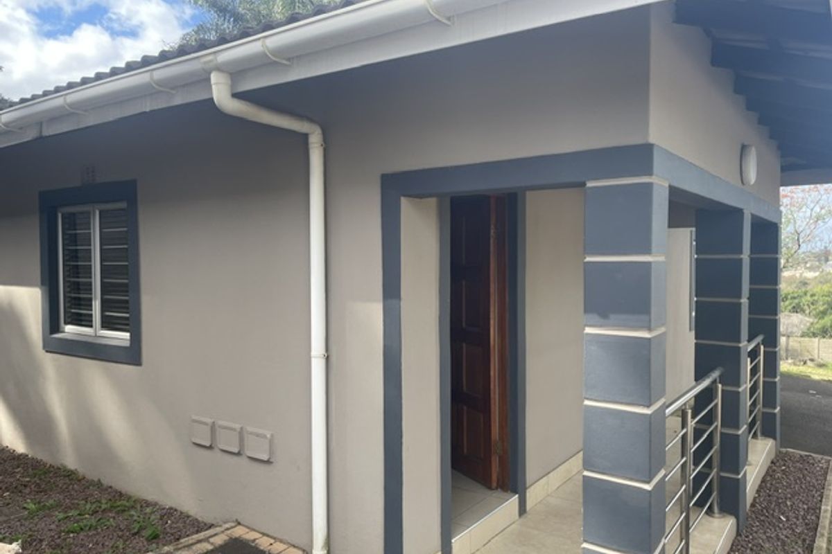A well-maintained townhouse exterior featuring a covered patio entrance, tiled flooring, stainless steel balustrades, and modern painted masonry finishes.