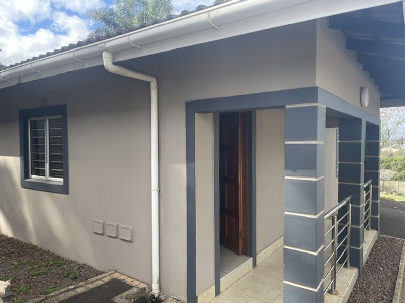 A well-maintained townhouse exterior featuring a covered patio entrance, tiled flooring, stainless steel balustrades, and modern painted masonry finishes.