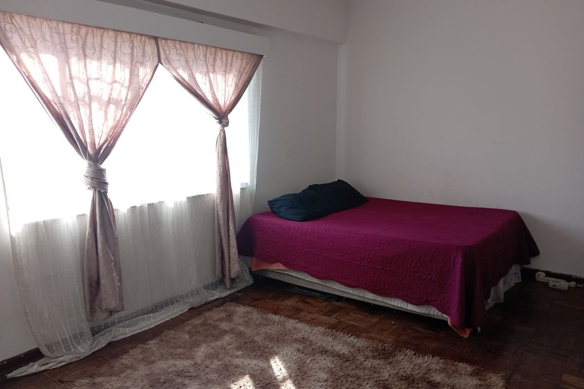 A bedroom featuring classic parquet flooring and a large window with installed curtain rails, providing a functional and well-lit living space.