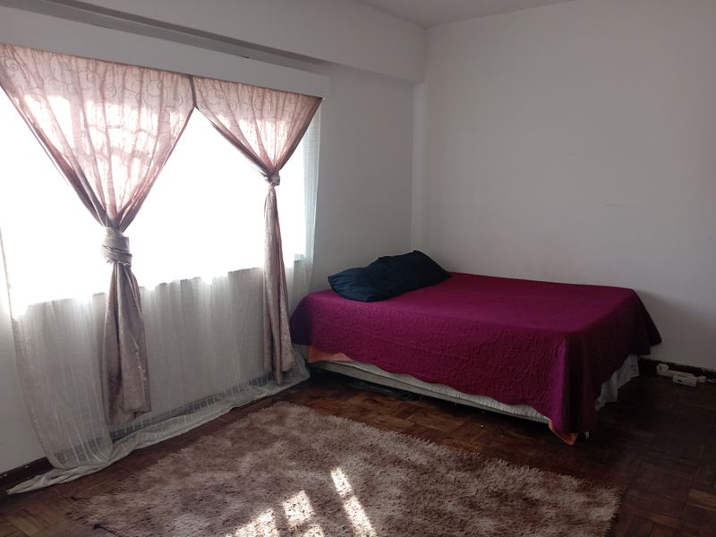A bedroom featuring classic parquet flooring and a large window with installed curtain rails, providing a functional and well-lit living space.