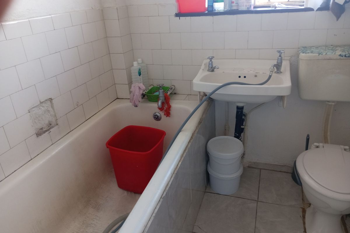 A dated bathroom featuring a bathtub, wall-mounted basin, and toilet, requiring significant renovation and cosmetic updates to improve its condition and functionality.