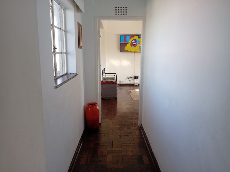 A hallway featuring classic parquet flooring and a steel-framed window, leading into an adjacent living space.