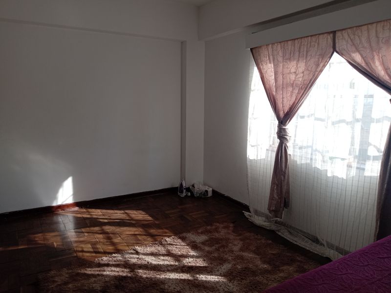A bright, empty bedroom featuring classic parquet flooring and large windows with installed curtain rails, offering a blank canvas for personalization.