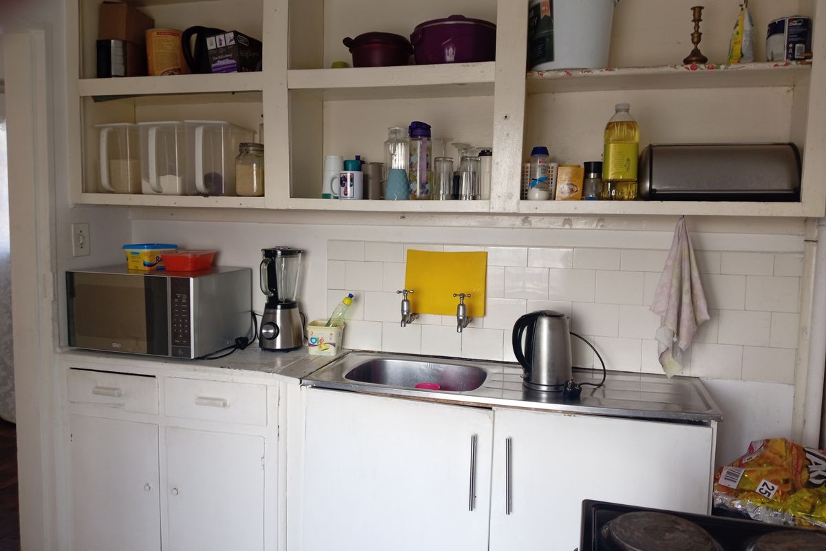 A functional kitchen area featuring white built-in cabinetry, open shelving, a stainless steel sink, and a tiled splashback.