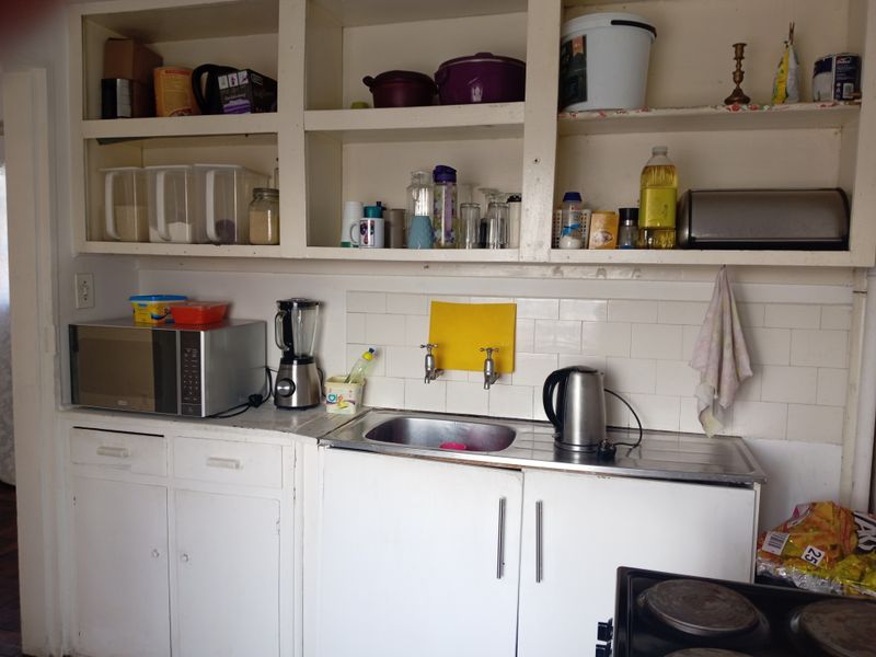 A functional kitchen area featuring white built-in cabinetry, open shelving, a stainless steel sink, and a tiled splashback.