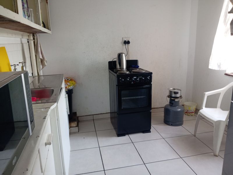 A functional kitchen area featuring tiled flooring, built-in cabinetry, a stainless steel sink, and a freestanding stove.