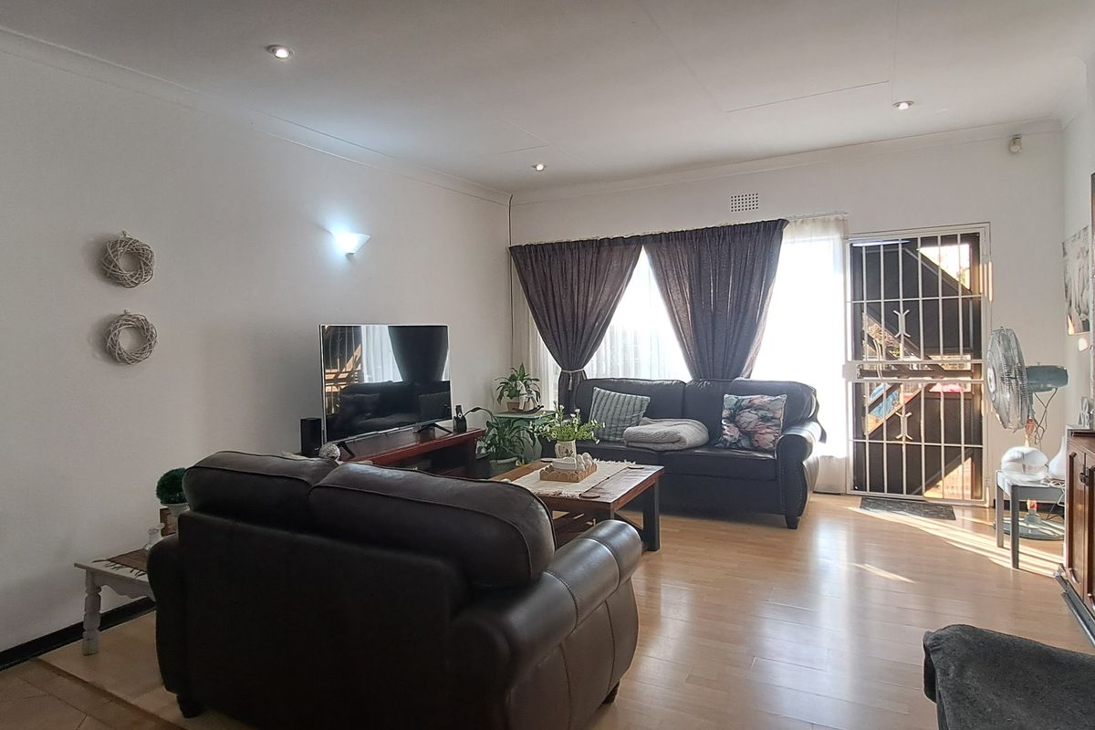 A spacious living room featuring laminate flooring, recessed downlighting, and a secure entrance door with a metal security gate.