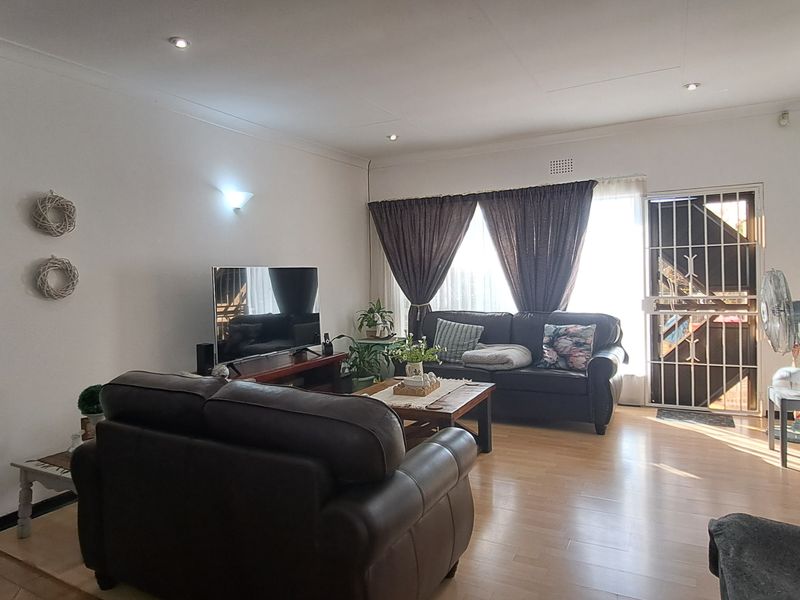 A spacious living room featuring laminate flooring, recessed downlighting, and a secure entrance door with a metal security gate.