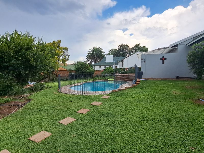 A backyard area featuring a swimming pool with safety fencing, surrounded by a well-maintained lawn and established garden landscaping.