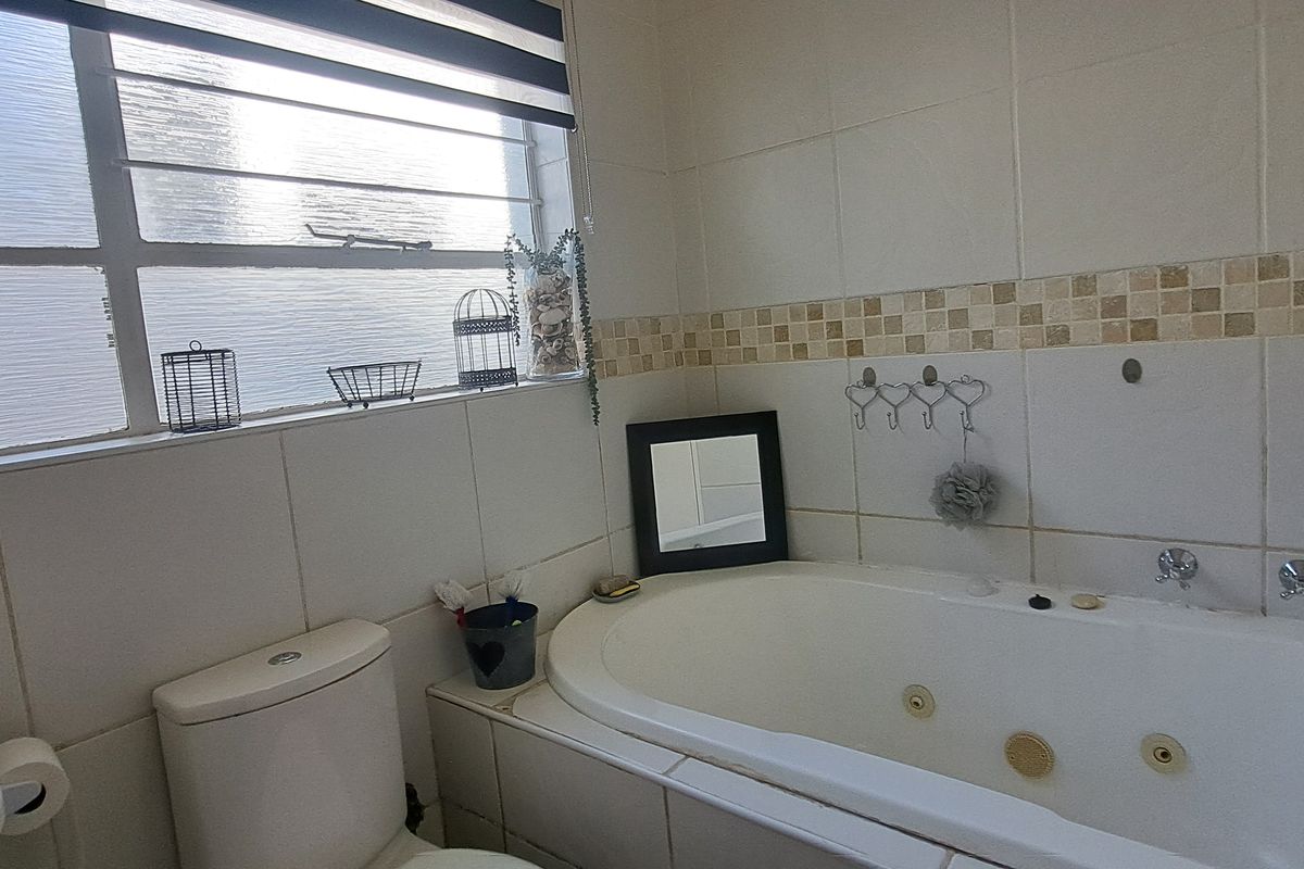 A functional bathroom featuring a built-in jetted bathtub, toilet, and tiled wall finishes with a window for natural light.